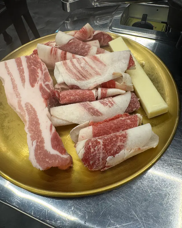 금빛 접시에 담겨 나온 신선한 흑돼지 오겹살과 곁들임 치즈