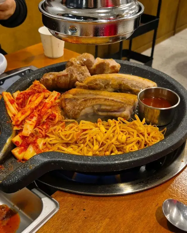 불판 위에 올려진 흑돼지 오겹살과 김치, 콩나물