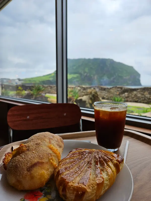 커피와 빵이 놓인 테이블, 창밖으로 성산일출봉이 보인다