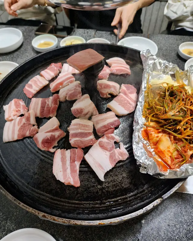 솥뚜껑 위에 올려진 오겹살과 김치