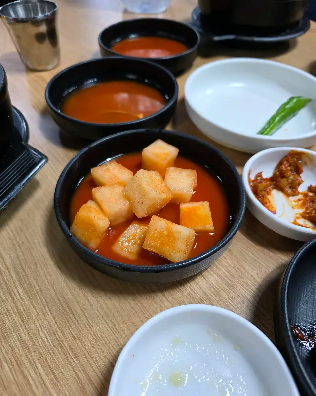 테이블 위에 놓인 깍두기, 고추, 다진 마늘 등의 반찬