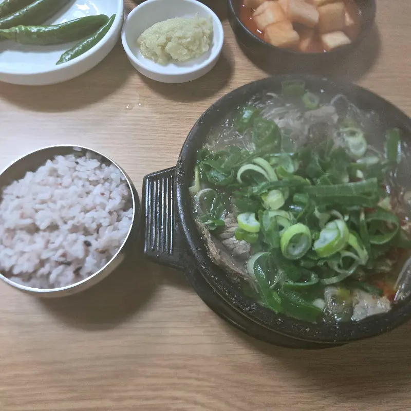 테이블 위에 놓인 해장국 뚝배기와 밥, 깍두기, 고추, 다진 마늘