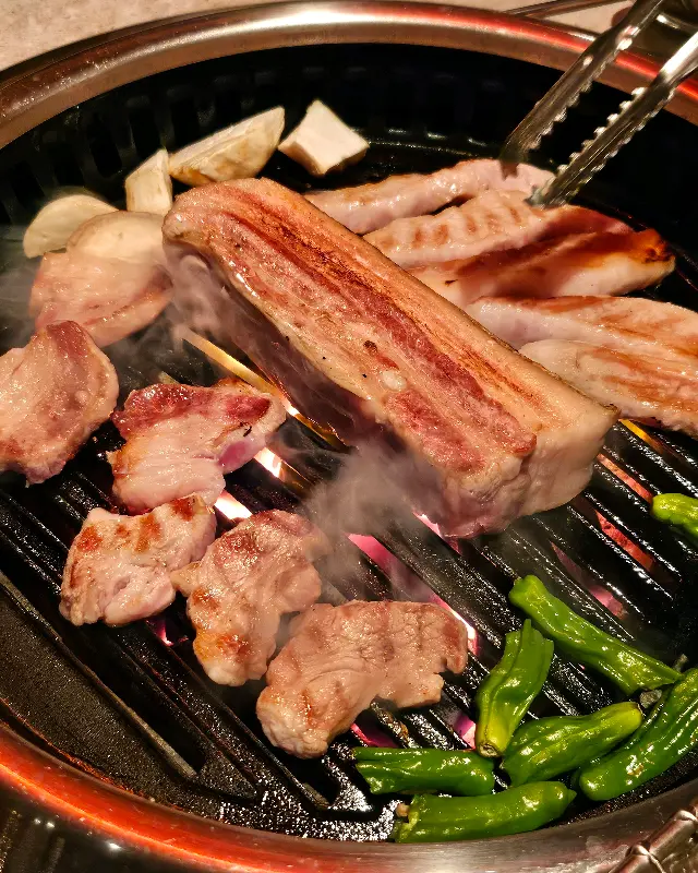 돈가도 불판 위에서 노릇하게 익어가는 흑돼지 오겹살과 마늘, 멜젓