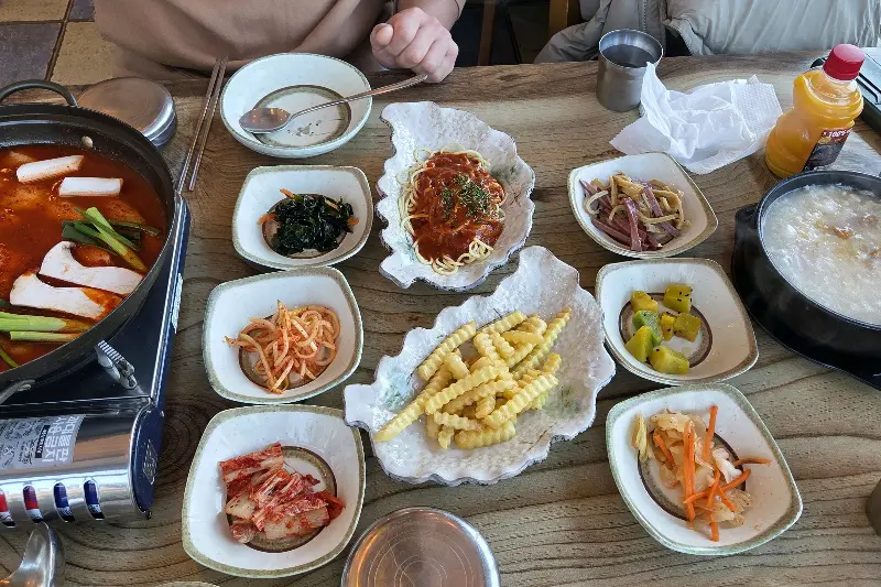 테이블 위에 놓인 갈치조림, 미역국, 김치, 스파게티, 감자튀김 등 다양한 음식들