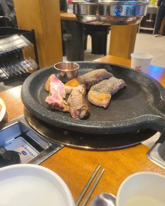 불판 위에 놓인 흑돼지 오겹살과 멜젓