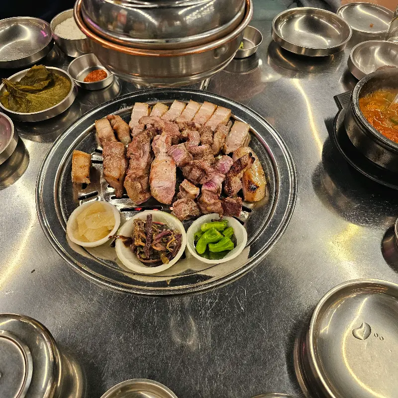 불판 위에 올려진 흑돼지 오겹살과 다양한 곁들임 찬