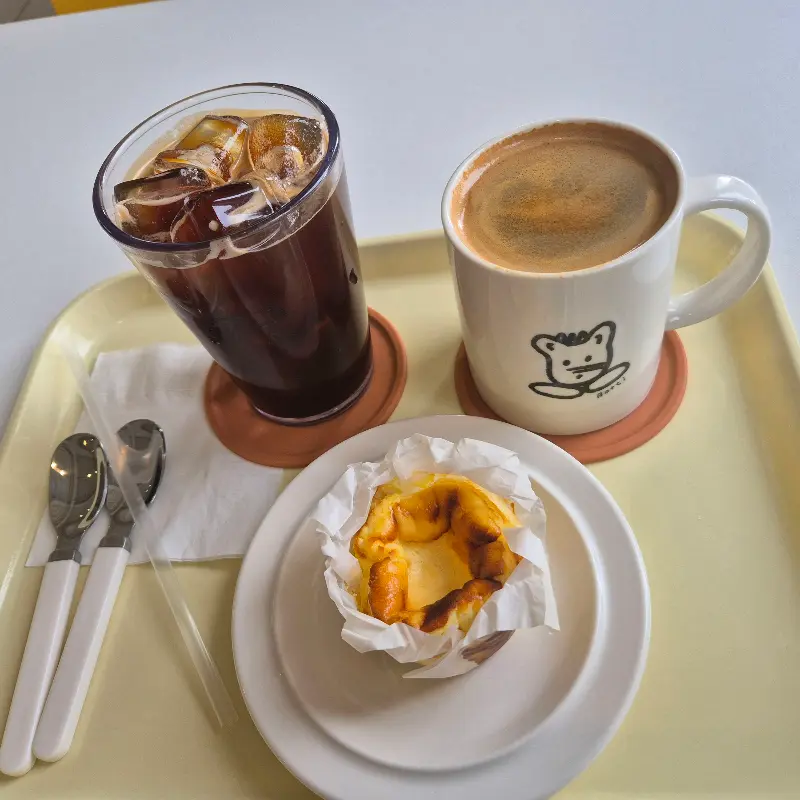 아이스 아메리카노와 따뜻한 아메리카노, 그리고 바스크 치즈 케이크가 쟁반 위에 놓여 있다.