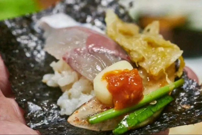 김 위에 밥, 고등어회, 묵은지, 양파, 특제 소스를 올려 한 입에 먹기 좋게 쌈을 만든 모습. 다채로운 색감이 식욕을 자극한다.