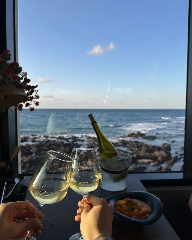 와인잔 두 개가 놓여 있고, 그 뒤로 제주 바다가 펼쳐진 모습