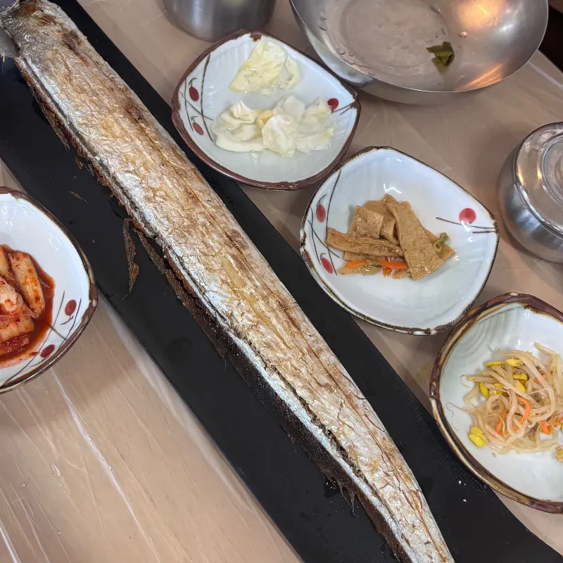 갈치구이와 갈치조림, 톳무침, 깻잎 장아찌 등 다양한 반찬들이 테이블 위에 가득 차려져 있다.