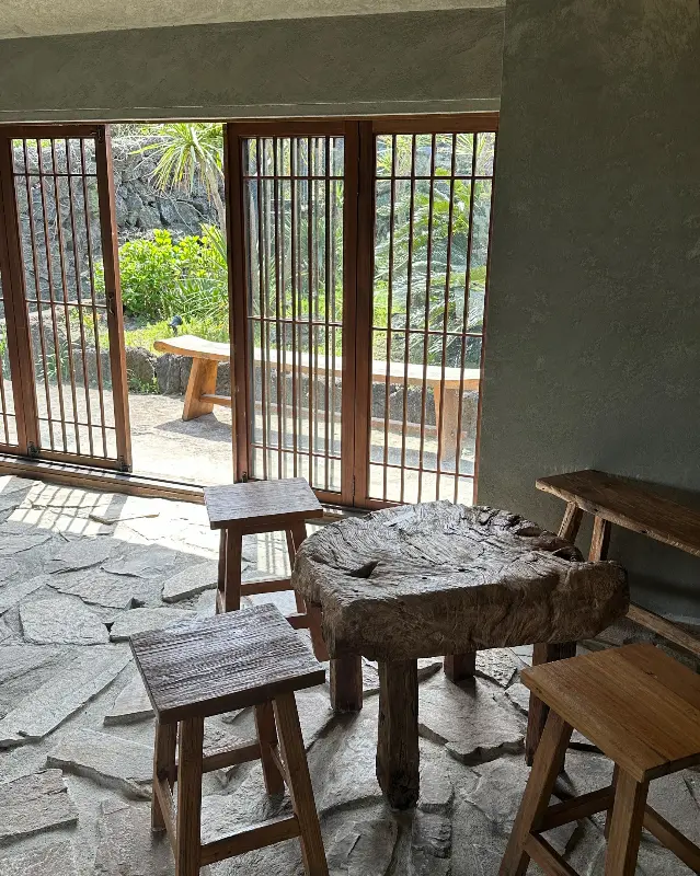 카페 내부, 나무 테이블과 의자가 놓여 있고, 창밖으로 햇살이 들어온다.