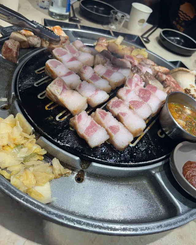 불판 위에 가지런히 놓인 삼겹살과 김치, 멜젓의 조화가 식욕을 자극한다.