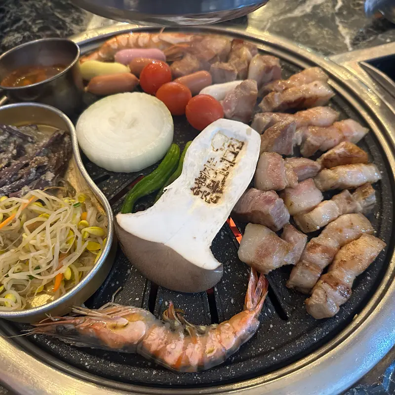 불판 위에 흑돼지 오겹살, 새우, 버섯 등이 구워지고 있는 모습