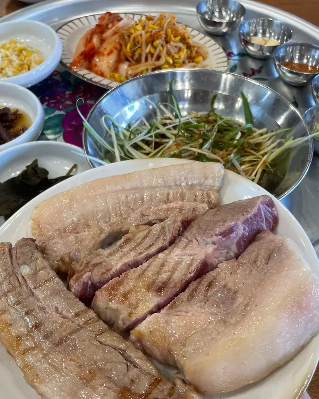 초벌된 흑돼지 오겹살과 다양한 밑반찬이 돌판 위에 올려져 있는 모습