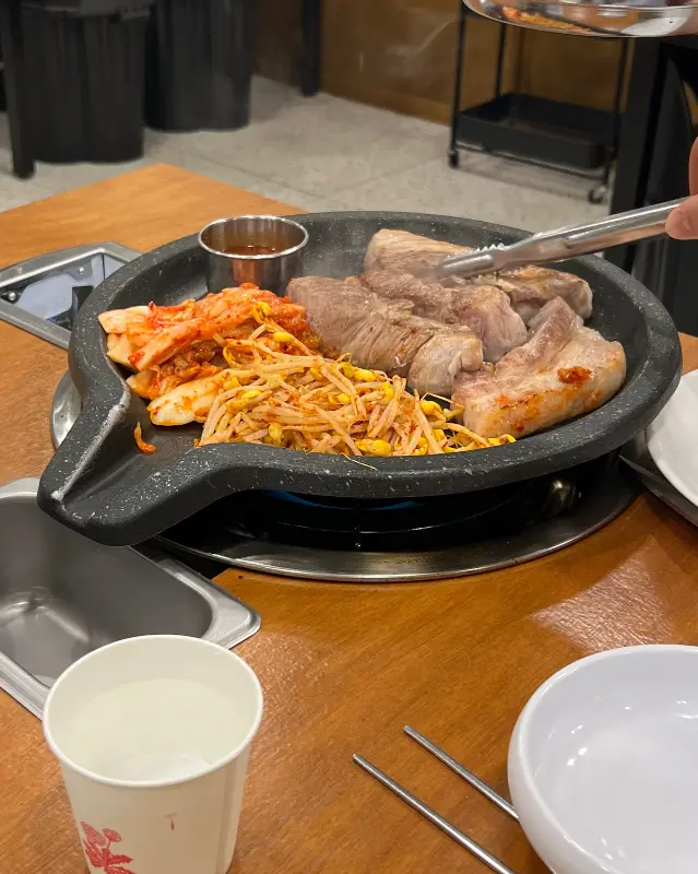 돌판 위에 구워진 흑돼지 오겹살과 김치, 콩나물의 모습