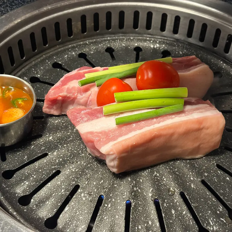 불판 위에 올려진 흑오겹살과 멜젓