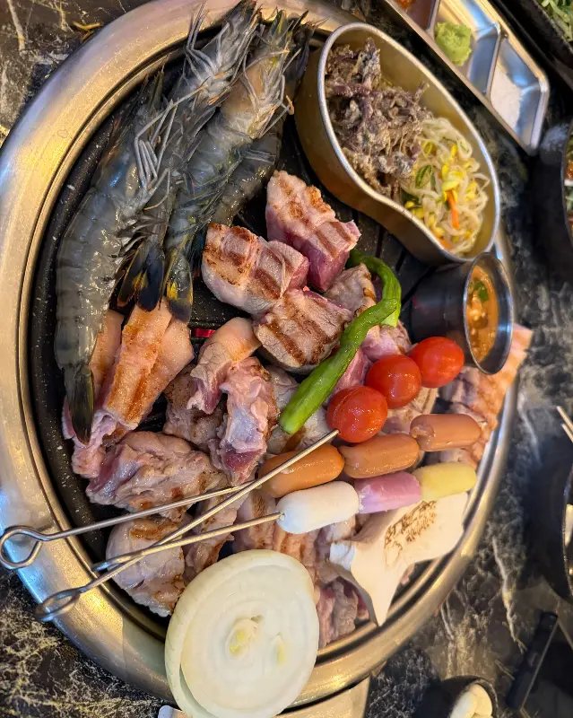 불판 위에서 익어가는 흑돼지, 새우, 소세지, 버섯, 양파