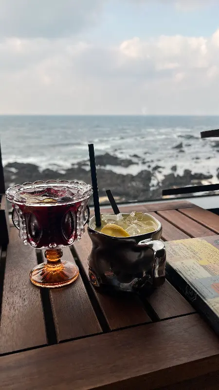 칵테일 두 잔이 테이블 위에 놓여 있고, 그 뒤로 제주 바다가 펼쳐진 모습