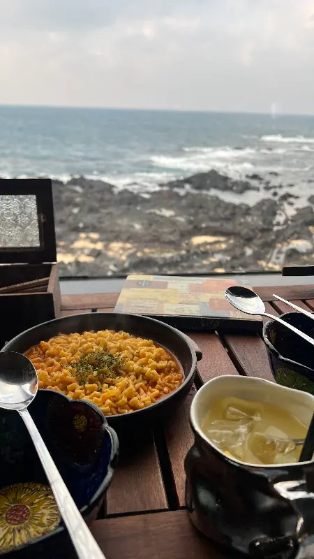 게딱지장 라면과 칵테일이 테이블 위에 놓여 있고, 그 뒤로 제주 바다가 보이는 모습