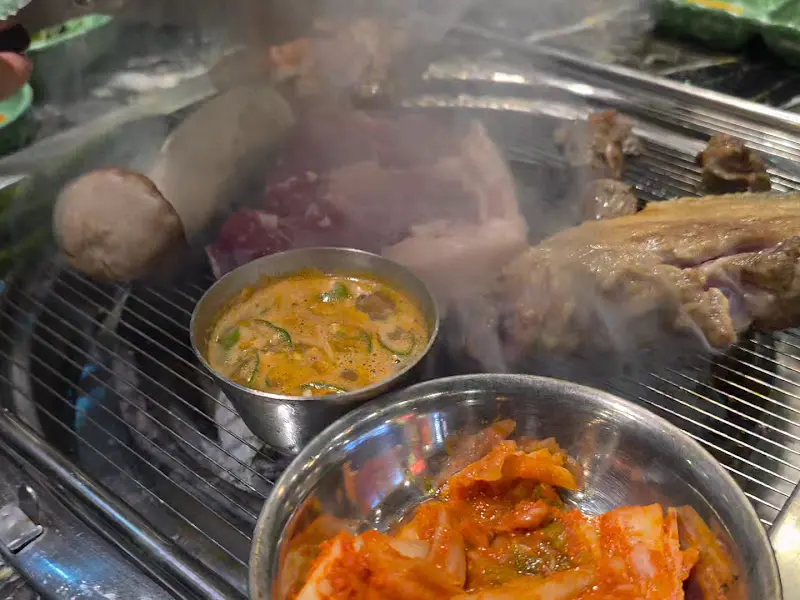 불판 위에서 연기를 내며 익어가는 흑돼지 오겹살과 멜젓