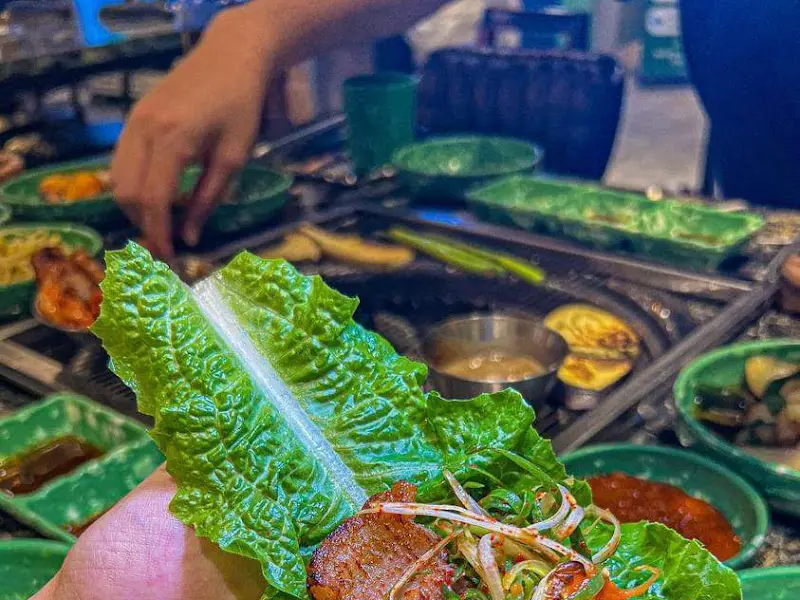 잘 익은 흑돼지 한 점을 쌈 채소와 함께 즐기는 모습