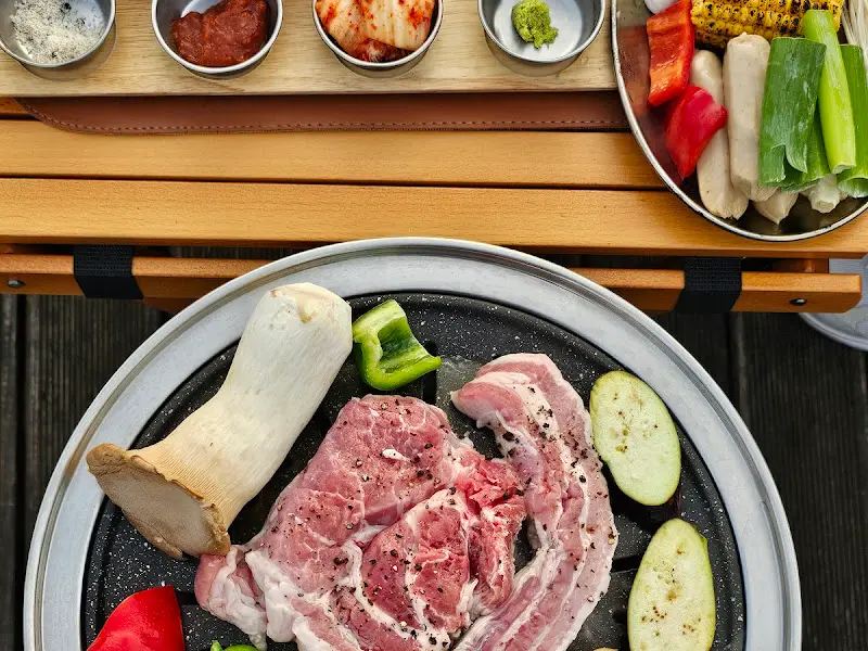 3단 트레이에 담겨 나온 밑반찬과 흑돼지, 버섯, 소세지 등 바베큐 재료들. 정갈하고 푸짐한 모습이 인상적이다.