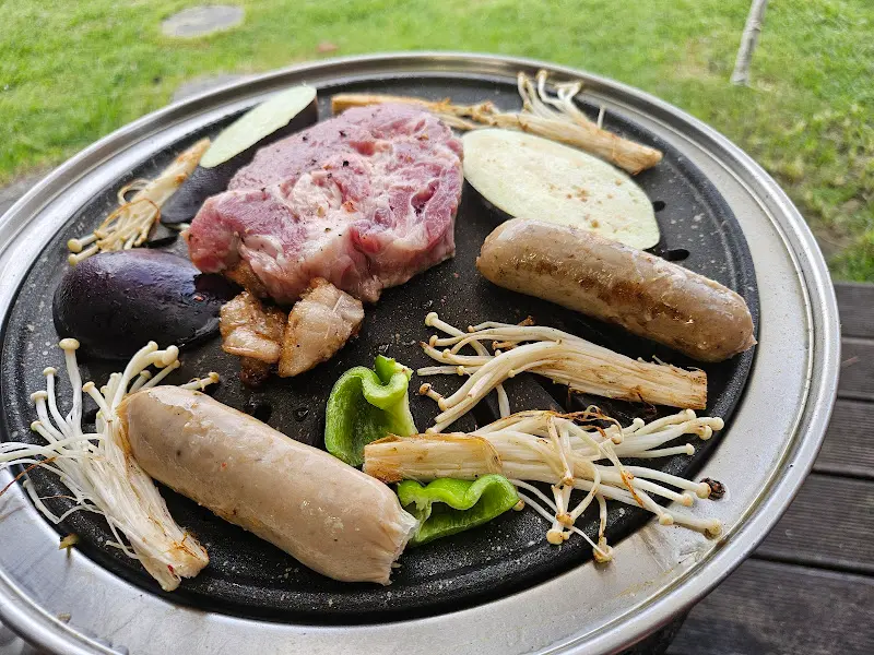 숯불 위에서 흑돼지 오겹살, 소세지, 버섯, 양파 등이 구워지고 있다.