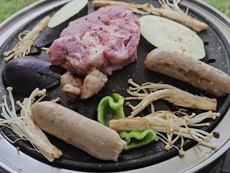 잘 익은 흑돼지 오겹살과 소세지, 버섯, 꽈리고추가 숯불 위에 놓여 있다.