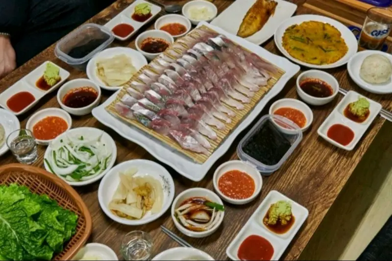 테이블 위에 푸짐하게 차려진 고등어회 한 상의 전체적인 모습. 다양한 곁들임 메뉴와 소스들이 함께 제공되어 풍성함을 더한다.