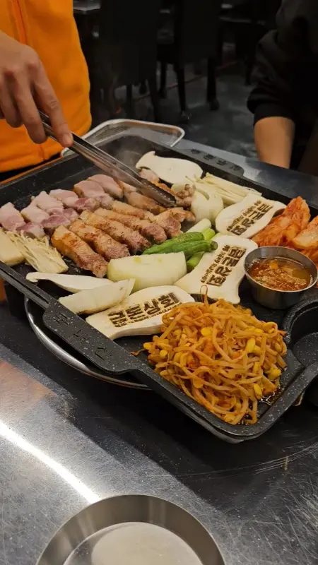 잘 구워진 흑돼지 오겹살과 김치를 함께 쌈으로 싸 먹는 모습