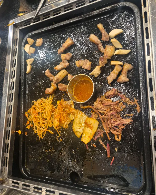 불판 위에 구워진 흑돼지, 김치, 콩나물, 멜젓