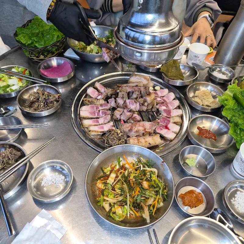 흑돼지 오겹살과 다양한 곁들임 메뉴들이 푸짐하게 차려진 테이블 모습