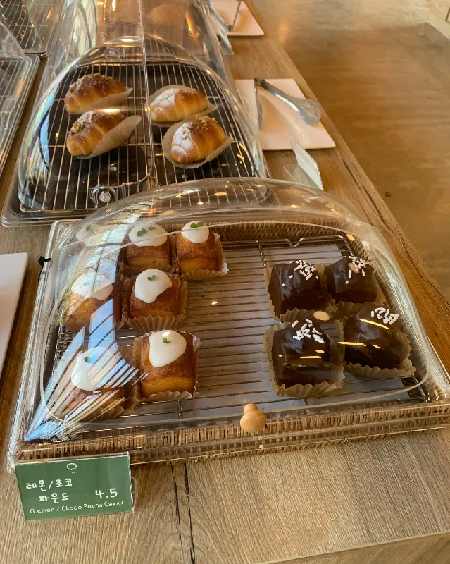 진열대 위에 놓인 다양한 종류의 빵들. 마농 소금빵, 레몬 초코 파운드 케이크 등이 보인다.