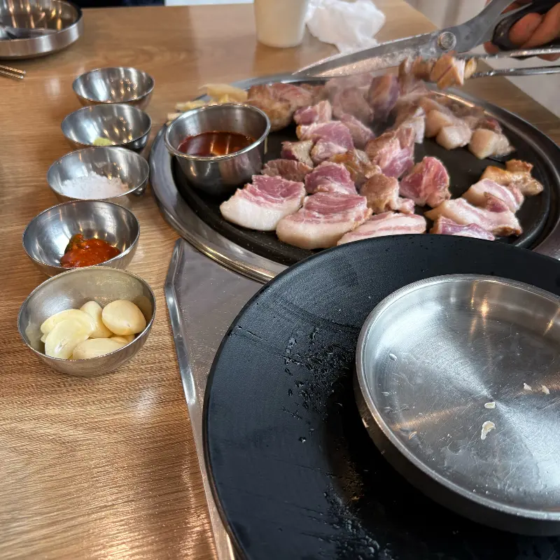 흑돼지 근고기와 다양한 소스, 밑반찬이 테이블 위에 놓여있는 모습