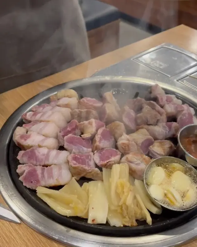 불판 위에 가득 올려진 흑돼지 근고기와 구워진 백김치의 모습