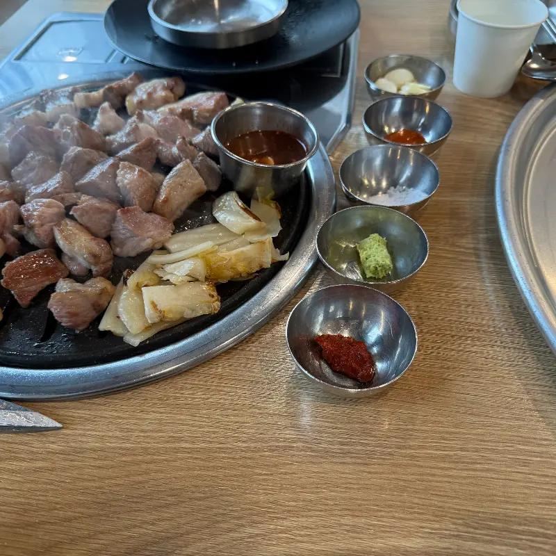 불판 위에 놓여진 흑돼지 근고기와 멜젓, 다양한 소스의 모습