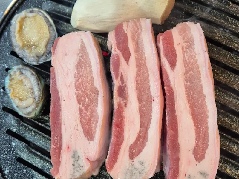 불판 위에 올려진 흑돼지 오겹살, 전복, 새송이버섯