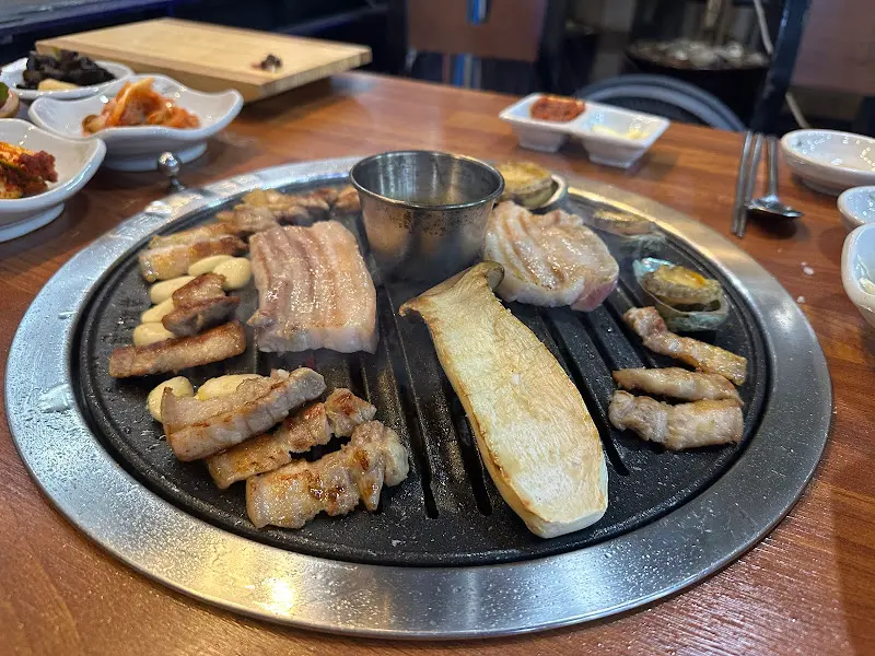 불판 위에서 맛있게 구워진 흑돼지 오겹살과 버섯