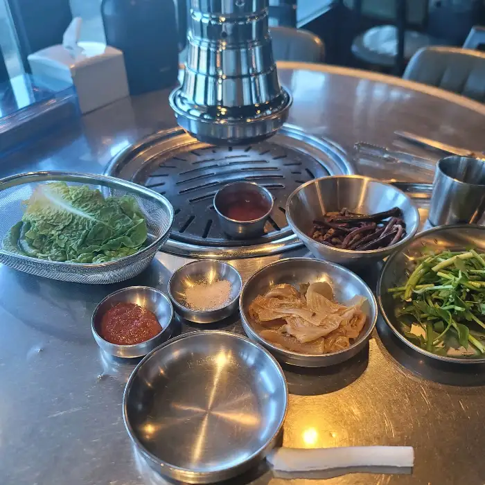 준비된 쌈 채소, 곁들임 찬, 그리고 멜젓이 담긴 앙증맞은 소스가 테이블에 놓인 모습