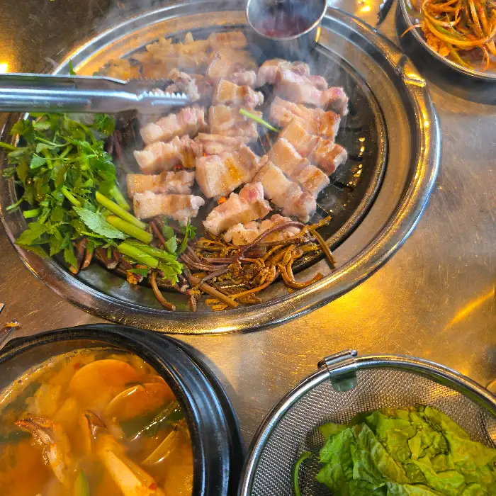 먹음직스럽게 구워진 흑돼지와 채소가 가득한 불판, 그리고 옆에는 해물 뚝배기가 보인다