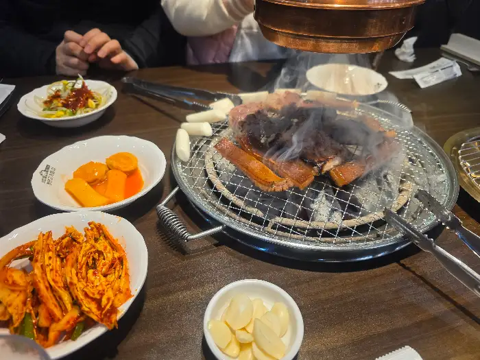 불판 위에서 구워지는 삼겹살과 곁들임 음식
