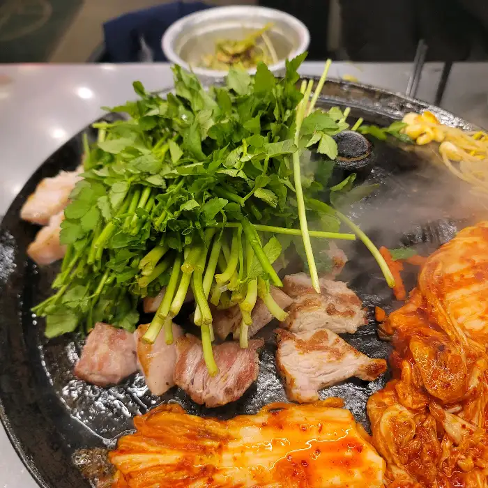 손으로 집게를 이용해 솥뚜껑 위 삼겹살을 뒤집는 모습
