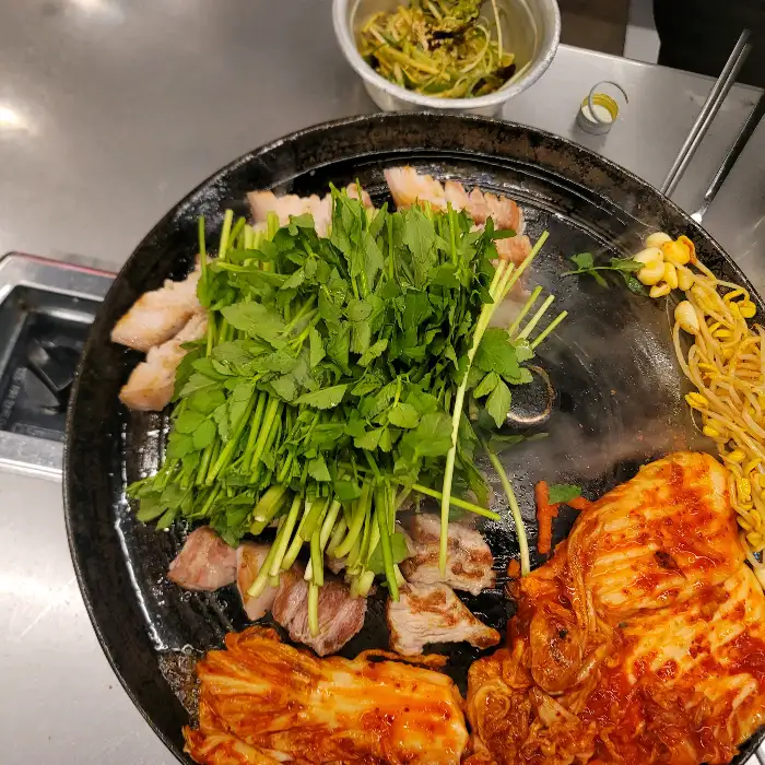 솥뚜껑 위에서 김치, 콩나물, 미나리와 함께 구워지는 삼겹살