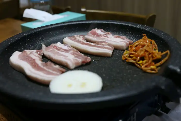 불판 위에 구워지고 있는 삼겹살과 콩나물 무침