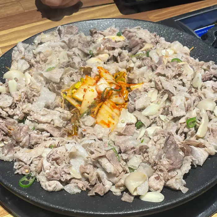 푸짐한 대패삼겹살과 함께 김치, 대파, 마늘 등이 볶아지고 있는 모습