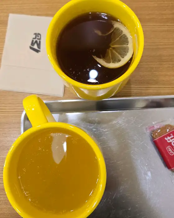 노란색 컵에 담긴 따뜻한 차와 레몬 슬라이스, 그리고 다른 컵에 담긴 음료