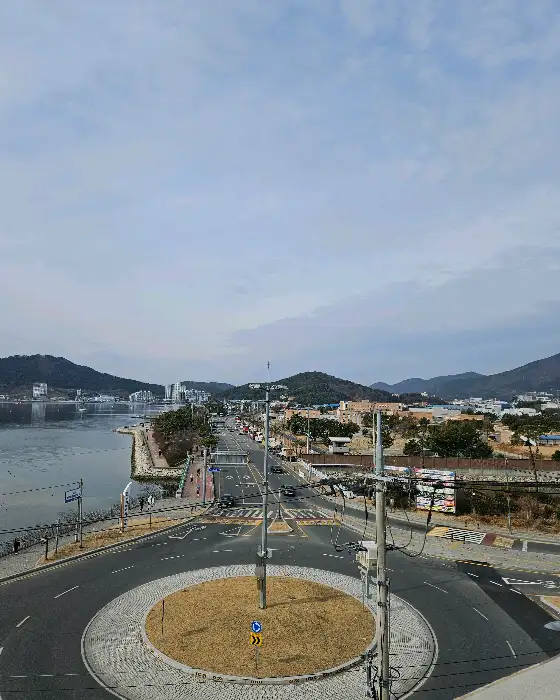 넓은 도로와 건물들이 보이는 도시 풍경, 멀리 산과 바다가 보이는 전경