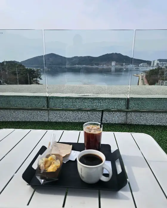 커피와 디저트가 놓인 테이블, 뒤로 바다가 보이는 풍경