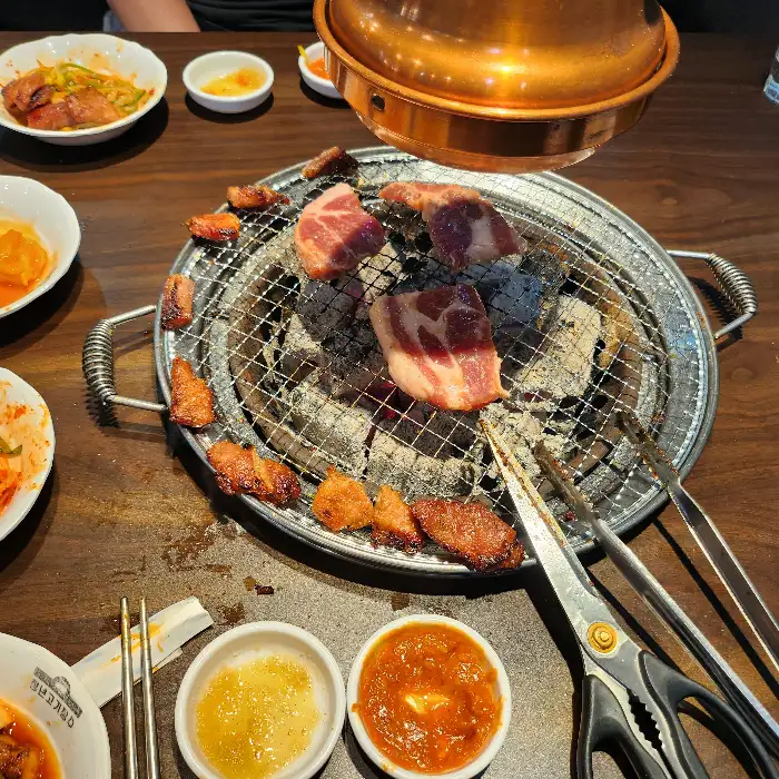 불판 위에서 노릇하게 익어가는 고기와 곁들임 음식