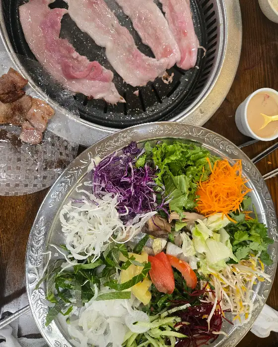 불판 위에서 익어가는 고기와 신선한 월남쌈 채소